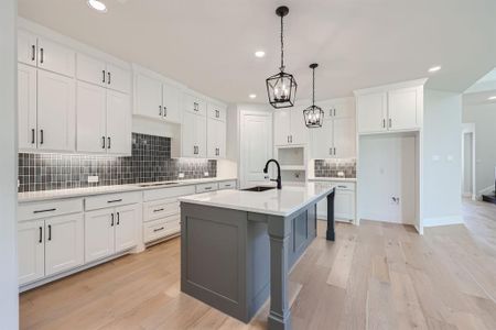 Kitchen with hanging light fixtures, white cabinets, decorative backsplash, a center island with sink, and light hardwood / wood-style floors