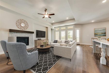 Living room with wood-type flooring, a stone fireplace, and ceiling fan