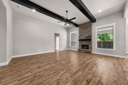 Unfurnished living room featuring beamed ceiling, ceiling fan, a stone fireplace, and wood-type flooring