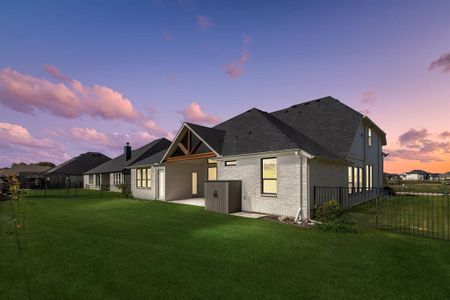 Back house at dusk featuring a lawn and a patio area