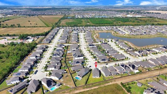 This aerial photo showcases a modern suburban development with neat rows of single-family homes, some waterfront properties near a man-made lake, and ample green space. The community is expansive, with more development in the distance, suggesting a growing area with potential for future amenities.