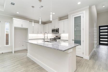 Kitchen with appliances with stainless steel finishes, white REAL WOOD cabinets, an island with sink, and light stone countertops