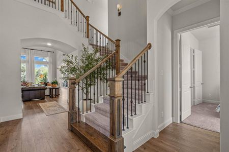 Stairs with a towering ceiling, crown molding, and hardwood / wood-style floors