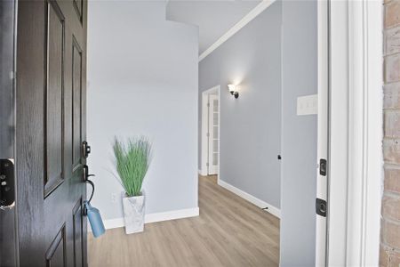 Entrance foyer with a coat closet, light laminate wood-style flooring and crown molding.
