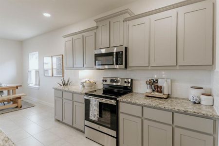 Kitchen featuring light tile patterned floors, gray cabinetry, backsplash, appliances with stainless steel finishes, and light stone countertops