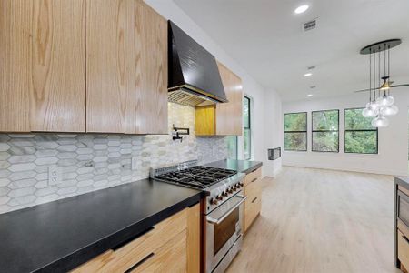 Kitchen with pendant lighting, high end range, backsplash, ventilation hood, and light hardwood / wood-style floors