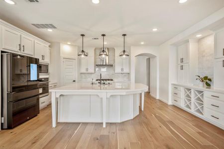 The kitchen boasts a deco wood paneled island with a sleek black faucet and large single basin sink. Upgraded with built-in stainless steel appliances, a 5 burner gas cooktop, above pendant lighting, and sleek white cabinets, this kitchen is ideal for cooking for the whole family or hosting holidays!