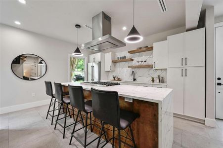 The kitchen island doubles as a dining area, offering a convenient and stylish space for meals and gatherings. Adorned with a combination of white marble countertops and wooden accents.