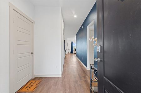 This well-lit hallway features beautiful premium laminate floors, a contrast of neutral and bold blue accent wall. The space is inviting with a view into adjacent rooms, suggesting an open and connected layout.
