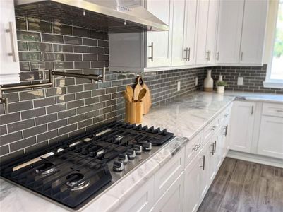 Kitchen with light stone counters, tasteful backsplash, black gas stovetop, dark wood-type flooring, and white cabinets