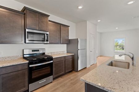 Kitchen with light wood-style flooring, light stone counters, sink, appliances with stainless steel finishes, and dark cabinetry