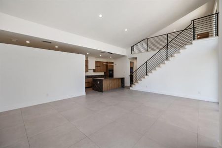 Modern open-concept living space with a sleek kitchen, large tiled floor, and a contemporary staircase with metal railings. Bright and airy with ample wall space for customization.