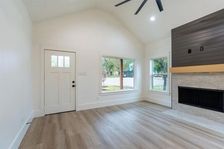 Unfurnished living room featuring light wood-type flooring, a fireplace, ceiling fan, and high vaulted ceiling