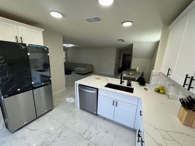 Kitchen with appliances with stainless steel finishes, white cabinets, light stone counters, sink, and light tile flooring