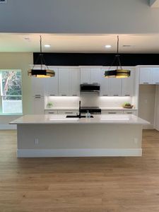 Kitchen featuring exhaust hood, an island with sink, hanging light fixtures, and white cabinets