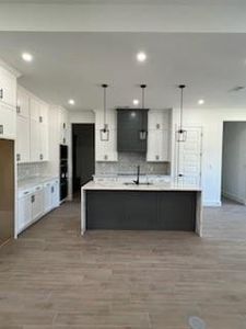 Kitchen with a center island with sink, hanging light fixtures, and white cabinetry