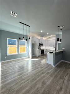 Kitchen featuring kitchen peninsula, appliances with stainless steel finishes, white cabinetry, hardwood / wood-style flooring, and decorative light fixtures