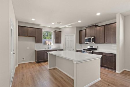 This light and bright kitchen features a large quartz island, dark stained cabinets, a large sink overlooking your backyard, recessed lighting, and beautiful backsplash.