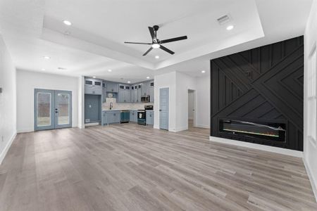 Unfurnished living room featuring ceiling fan, a fireplace, a raised ceiling, and light hardwood / wood-style flooring