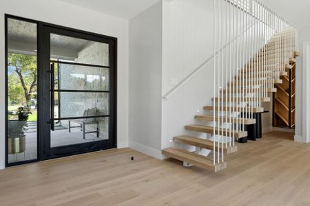 Oversized steel pivot door with floating staircase and wine storage at the ample entry way.