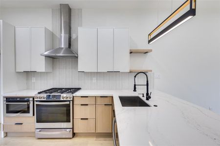 Kitchen featuring light wood-type flooring, sink, wall chimney range hood, appliances with stainless steel finishes, and light brown cabinetry