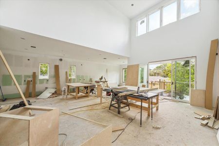 Just beyond the foyer is a large family room with mirroring 20 ft ceilings, large picture windows, sliding glass doors, and an open concept to the kitchen and dining area. Photo as of 7/30/24