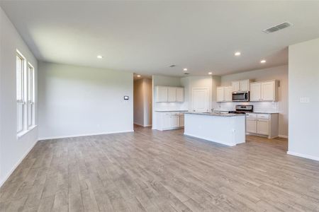 Kitchen featuring light hardwood / wood-style floors, an island with sink, white cabinets, stone counters, and stainless steel appliances