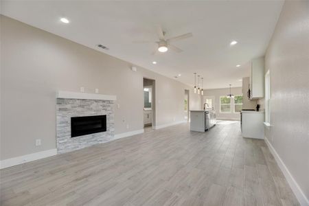 Unfurnished living room featuring a stone fireplace, sink, ceiling fan, and light ceramic tile hardwood / wood-style floors