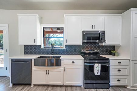 Kitchen featuring backsplash, sink, appliances with stainless steel finishes, and white cabinets