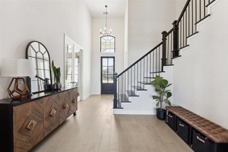 Another view of the light and airy entryway with a high ceiling and elegant staircase. The space creates a welcoming atmosphere and the front door with glass panels lets in natural light, enhancing the open feel of the home.