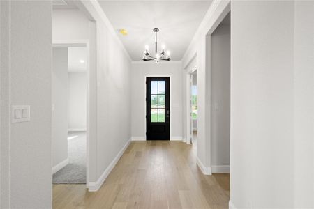 Entrance foyer with light wood-type flooring, crown molding, and a notable chandelier