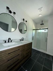 Bathroom featuring tile floors, dual bowl vanity, and a shower with shower door