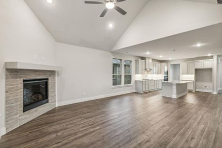 Unfurnished living room featuring high vaulted ceiling, wood-type flooring, a tile fireplace, and ceiling fan