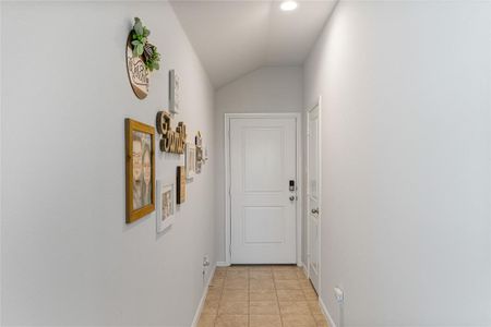 Hallway with vaulted ceiling and light tile patterned floors