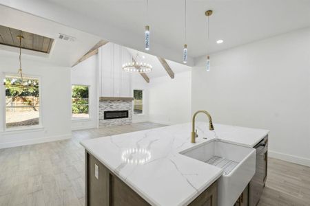 Kitchen featuring vaulted ceiling with beams, hanging light fixtures, light hardwood / wood-style floors, light stone counters, and a kitchen island with sink