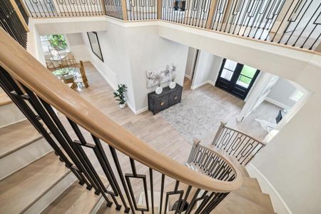 This is transitional two-story home features an open foyer with high ceilings, elegant wooden stairs with black wrought iron balusters, ample natural light, and a view into the adjacent rooms, showcasing a stylish and spacious interior, perfect for entertaining.