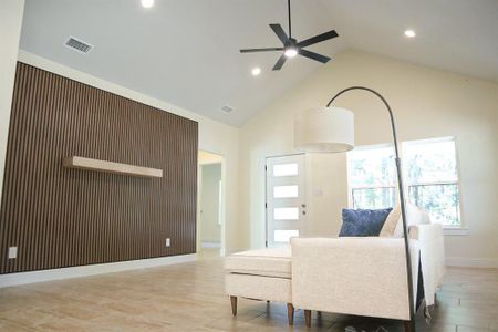 Living room with ceiling fan, high vaulted ceiling, and wood walls