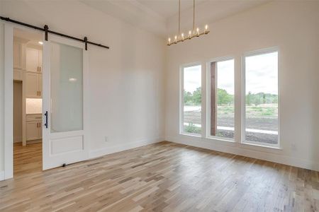 Unfurnished room with light hardwood / wood-style flooring, a barn door, and an inviting chandelier