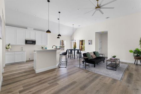 Kitchen featuring wood-type flooring, an island with sink, hanging light fixtures, white cabinetry, and lofted ceiling