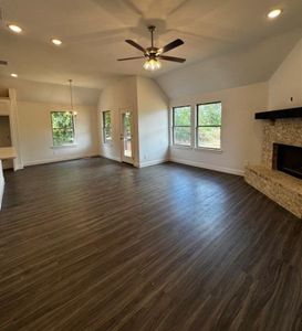 Unfurnished living room featuring ceiling fan with notable chandelier, lofted ceiling, dark wood-type flooring, and a stone fireplace