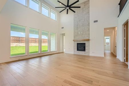 Unfurnished living room with a tile fireplace, ceiling fan, light hardwood / wood-style flooring, and a towering ceiling