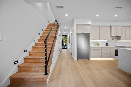 Kitchen with white cabinets, oven, light wood-type flooring, and stainless steel fridge