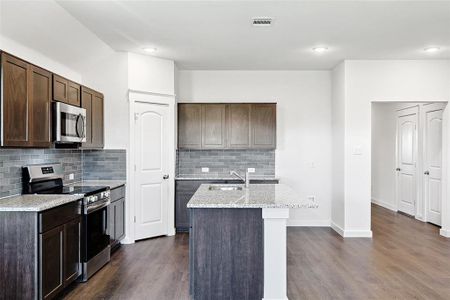 Kitchen with appliances with stainless steel finishes, dark hardwood / wood-style floors, an island with sink, and dark brown cabinetry