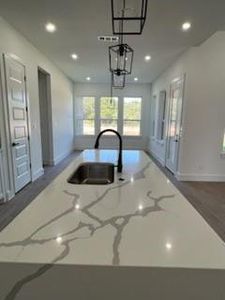 Kitchen with pendant lighting, dark hardwood / wood-style flooring, a center island with sink, sink, and light stone countertops