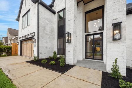 This stunning home features a limewashed brick exerior, custom wood garage door and covered front porch with contemporary  iron framed glass doors.