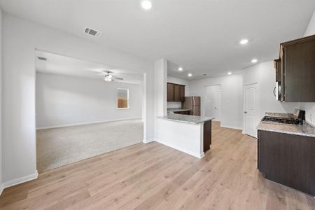 Kitchen featuring appliances with stainless steel finishes, light stone counters, light hardwood / wood-style floors, kitchen peninsula, and ceiling fan