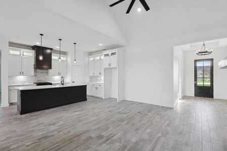 Kitchen with an island with sink, lofted ceiling, hanging light fixtures, custom range hood, and light hardwood / wood-style floors