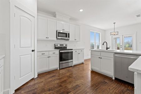 Kitchen with white cabinets, hanging light fixtures, appliances with stainless steel finishes, sink, and dark hardwood / wood-style floors