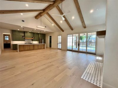 Unfurnished living room with high vaulted ceiling, beam ceiling, ceiling fan, and light hardwood / wood-style floors