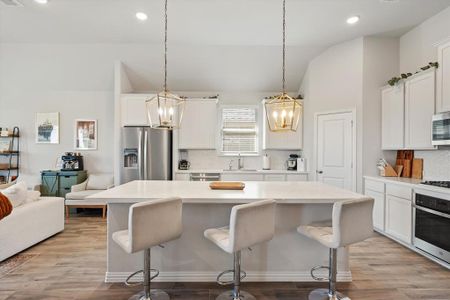 Oversized kitchen island with quartz counter tops, pendant lights, and custom white cabinets